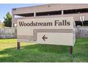 Exterior shot of the Woodstream Falls community sign with directional arrow, set against green grass at 9995 E Harvard Ave # 221, Denver, CO 80231