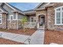 Inviting front entrance with a charming porch, stone accents, and manicured landscaping at 9727 Red Primrose St, Franktown, CO 80116