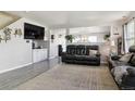 Bright living room with gray wood floors, a large black leather sofa, and decoratively-adorned wall at 765 Mockingbird St, Brighton, CO 80601