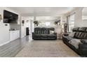 Open-concept living room with gray wood floors, a large black leather sofa, and plenty of natural light at 765 Mockingbird St, Brighton, CO 80601
