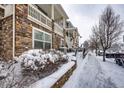 Stone-clad townhome with snow-covered walkway, front bush, and private porch, offering a cozy and inviting exterior at 9381 Ashbury Cir # 102, Parker, CO 80134