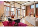 Spacious living room featuring exposed brick, hardwood floors, large windows, and a dining table at 1720 Wazee St # 3B, Denver, CO 80202