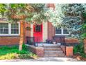Charming red brick condo entrance with a vibrant red door, surrounded by lush greenery and decorative plants at 1365 N Corona St # 11, Denver, CO 80218