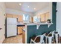 Eat-in kitchen bar area with adjacent white appliances, light wood cabinets, and stylish stools at 85 Uinta Way # 702, Denver, CO 80230