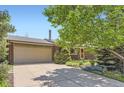 This home features a brick facade, attached two-car garage, and mature trees in a well-maintained front yard at 8292 E Lehigh Dr, Denver, CO 80237