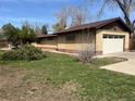 Side view of home with attached garage, brick exterior, green grass, and concrete walkway to the front at 5600 Dover St, Arvada, CO 80002