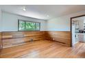 Spacious room with hardwood floors, wood-paneled walls, and a bright window that offers a view to the outdoors at 5600 Dover St, Arvada, CO 80002