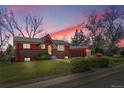 Charming red and brick home with lush green lawn and mature trees at sunset at 10978 W Ada Pl, Lakewood, CO 80226