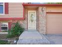 Close-up of a home's front entry with brick accents, a storm door, and colorful flowering bushes at 11112 Dahlia Way, Thornton, CO 80233
