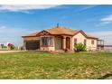 Beautiful home with brown roof and red trim surrounded by green grass at 46303 E 106Th Ave, Bennett, CO 80102