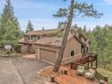 Exterior home features a two-car garage, basketball hoop, and large wooden deck with outdoor seating at 3726 Spring Valley Trl, Evergreen, CO 80439