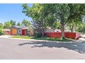 View of a modern single-story home with a red front door and fence surrounded by mature trees at 5480 W Iowa Ave, Lakewood, CO 80232
