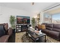 A living room has a brown leather couch, a dark wood floor, and a big window with sunlight at 25064 E Archer Pl, Aurora, CO 80018