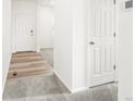 Hallway featuring light wood floors transitioning to carpet, with white doors and walls at 6074 Hourglass Dr, Brighton, CO 80601