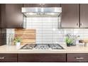 Modern gas range with stainless steel hood, white subway tile backsplash, and dark wood cabinets in a kitchen at 6723 Raritan Dr, Denver, CO 80221