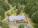 Aerial view of brick home with large deck, surrounded by lush trees and a stone retaining wall at 7815 Armadillo Trl, Evergreen, CO 80439