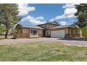 Inviting tan home with stone accents, two-car garage, mature trees, and gravel driveway at 1866 Mountain View St, Erie, CO 80516