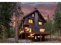 The charming house with a large deck and garage below is set amidst a tranquil forest backdrop at twilight at 592 Brook Dr, Idaho Springs, CO 80452