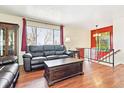 Open-concept living room with hardwood floors, black leather sofas, red accent wall, and natural light from a large window at 3310 W Mountain Rd, Englewood, CO 80110