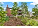 Charming brick two-story home featuring a covered front porch, landscaped garden, and mature trees at 2210 Miller St, Lakewood, CO 80215