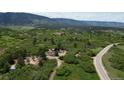 Wide shot of the property on a sprawling green landscape, featuring a small house near a winding road at 8821 S Perry Park Rd, Larkspur, CO 80118