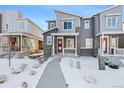 Two-story townhome with gray siding, red door, and snow-covered walkway at 23527 E 5Th Pl, Aurora, CO 80018