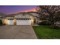 Charming home featuring a three car garage, brick accents, well-maintained landscaping, and a beautiful sky at dusk at 22778 E Alamo Ln, Aurora, CO 80015