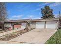 Home with a multi-car garage, brick accents, and a front yard with mature trees under a bright blue sky at 10983 W Exposition Pl, Lakewood, CO 80226