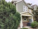 Exterior view of a two-story townhome featuring neutral siding, brick accents, and lush evergreens near the entry at 11947 Riverstone Cir # 7F, Henderson, CO 80640