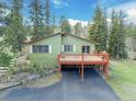 Back of a light green home with a dark red balcony, surrounded by lush greenery and a dark driveway at 8473 Gray Fox Dr, Evergreen, CO 80439