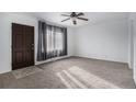 Bright living room with neutral carpet, ceiling fan, and a large window draped with elegant gray curtains at 7971 Olive St, Commerce City, CO 80022