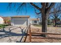 Exterior view of a grey home with a two-car garage, complemented by mature trees and a split-rail fence at 19000 E Mansfield Dr, Aurora, CO 80013