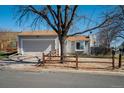 Home with grey exterior, two-car garage, front lawn, and beautiful shade tree with a split rail fence at 19000 E Mansfield Dr, Aurora, CO 80013