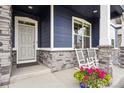 Close-up of charming blue home's front porch with grey door, stone columns, and rocking chairs at 8888 Falcon St, Longmont, CO 80504