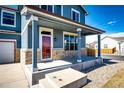 Inviting front porch with brick accents, sturdy columns, and a brightly colored front door at 2091 Basil St, Strasburg, CO 80136