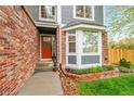 Welcoming front entrance featuring a brick facade, a vibrant orange door, and beautiful landscaping with a bay window at 1101 Ridgeview Cir, Broomfield, CO 80020