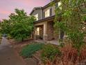 Charming home featuring a stone facade, covered front porch, and beautifully landscaped front yard with mature trees and plants at 14823 W 70Th Dr # A, Arvada, CO 80007