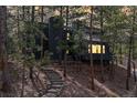 Modern mountain home at dusk nestled among mature trees with light glowing inside at 4966 Delaware Dr, Larkspur, CO 80118