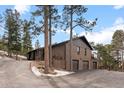 Brick home with a three-car garage and a side view featuring mature trees at 7845 Armadillo Trl, Evergreen, CO 80439