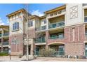 Three-story condo building with brick and siding, and green balconies on a sunny day at 9481 E Mansfield Ave # 203, Aurora, CO 80014