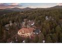 Areal view of home nestled in wooded area with sunset sky and mountain views at 21016 Horse Bit Way, Morrison, CO 80465