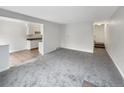 An empty living room featuring neutral carpet, paint, and entryway to kitchen and stairs at 9976 Appletree Pl, Thornton, CO 80260