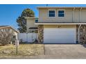 Tan two-story home featuring a two-car garage, white fence, and green grass at 2446 S Vaughn Way # A, Aurora, CO 80014