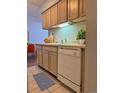 Compact kitchen featuring light wood cabinetry, white dishwasher, and tiled flooring at 7755 E Quincy Ave # 203A6, Denver, CO 80237