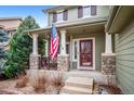 Cozy front porch with stone pillars, railings, and American flag at 9882 S Hoyt Ct, Littleton, CO 80127