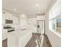Sun-filled kitchen with stainless steel appliances, white cabinets, island with double sink and wood-look floors at 1935 Coolidge Way, Aurora, CO 80018