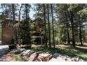 Quaint mountain home exterior showcasing natural wood, wooded lot and rock border with street sign at 11526 Green Cir, Conifer, CO 80433