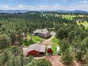 Wide aerial shot showcases the home, barn, and outbuildings surrounded by a dense forest landscape at 20125 Indi Dr, Monument, CO 80132