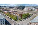 An aerial view displays modern condominiums with balconies and street parking, set against a backdrop of cityscape and mountains at 3295 Blake St # 301, Denver, CO 80205