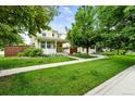 Well-manicured lawn with lush trees surrounding a charming home with a welcoming front porch at 2648 Florence St, Denver, CO 80238